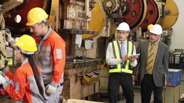 Audit crates on the factory floor anchor four people who stand comparing the morning output of stamped steel parts