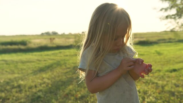Boy inspecting hand for splinter then walking through green field with lens flare
