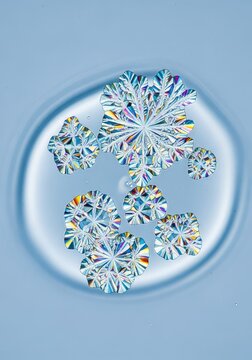 Microscopic view of shimmering crystalline cellular structures growing within a serene pale blue laboratory liquid in an abstract display, organic, pharmaceutical, futuristic