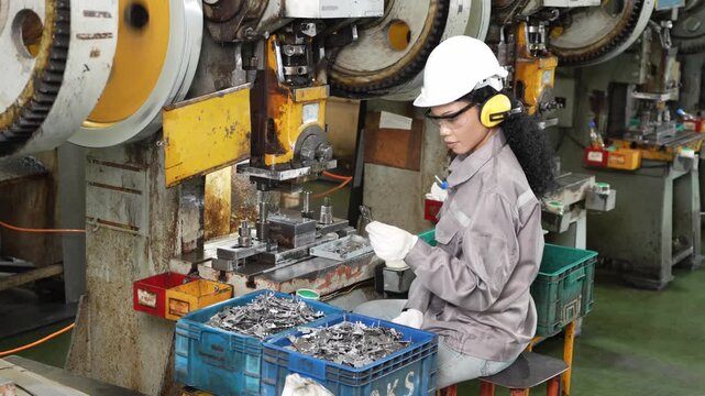 Another press stamping cycle runs through as the operator loads blanks by hand beside a crate of finished parts