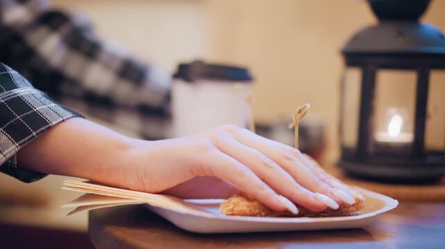 Woman hand reaches for and lifts sandwich from plate revealing action of picking up food. scene includes additional sandwiches on white paper tray with toothpicks napkins under main subject
