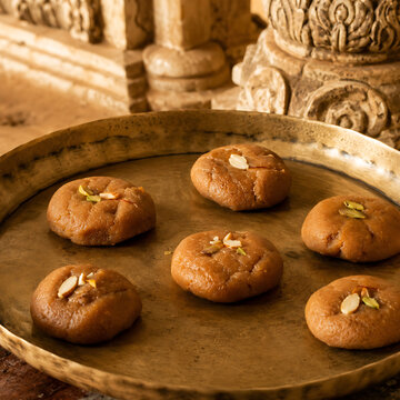 Traditional Mathura peda with characteristic caramel-brown surface and hand-shaped irregularities, arranged sparsely on an aged brass thali.