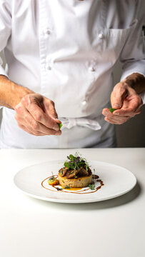 Professional chef in clean white uniform carefully plating gourmet dish in modern kitchen studio, precise hand movement and fine dining presentation, elegant food styling with microgreens.
