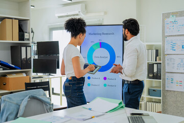 Obraz na płótnie Canvas Two colleagues analyzing marketing research data on digital screen, woman using tablet while male coworker reviews pie chart results, teamwork and data driven business strategy discussion in modern 
