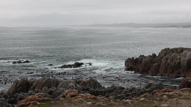 man wearing hat overlooking stormy dawn clouds over rocky coastline of DeKelders, South Africa