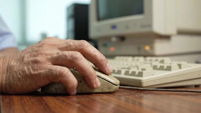Close up of hand clicking on old computer mouse near keyboard at desk in office setting during work hours