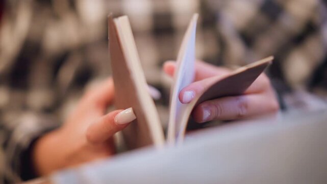Close up of person flipping through pages of notebooks with white nail polish on their hands. focus remains consistently sharp as they interact with multiple thin paper objects set