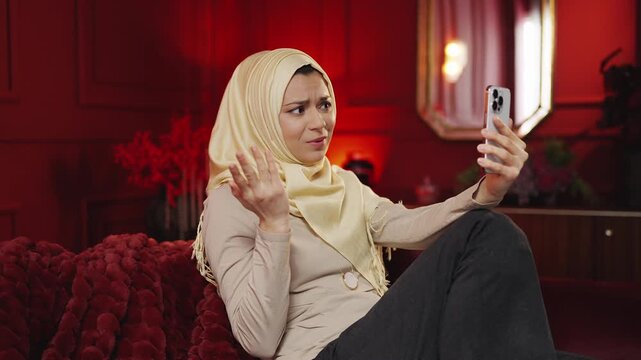 Young Muslim woman in hijab talks to friend during video call on smartphone