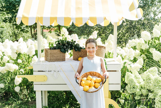 Smiling Girl Holding Basket of Fresh Lemons at Outdoor Summer Market