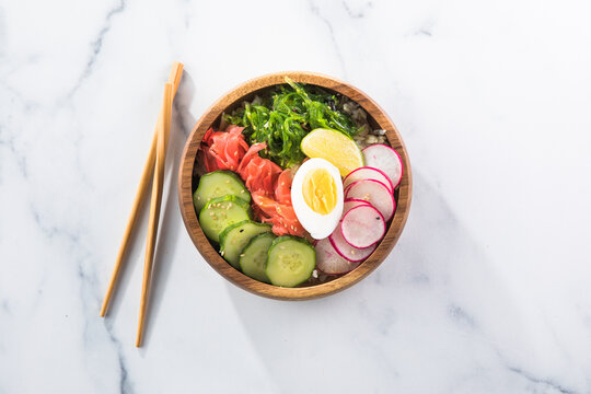 Overhead view of a colorful vegan poke bowl with rice, egg, gimnger, seaweed, radish, and veggies