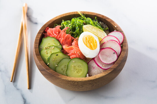 Overhead view of a colorful vegan poke bowl with rice, egg, gimnger, seaweed, radish, and veggies