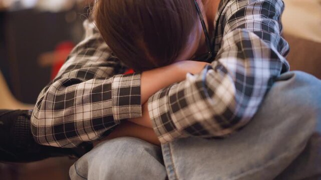 Close up of young girl wearing glasses resting her head on folded arms while sitting. Girl is dressed in plaid shirt and jeans with soft lighting creating warm tones. background remains
