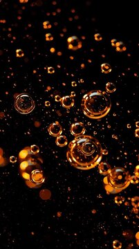 Droplets of oil are suspended in dark water, creating an amber glow as they move and reflect light in captivating patterns.
