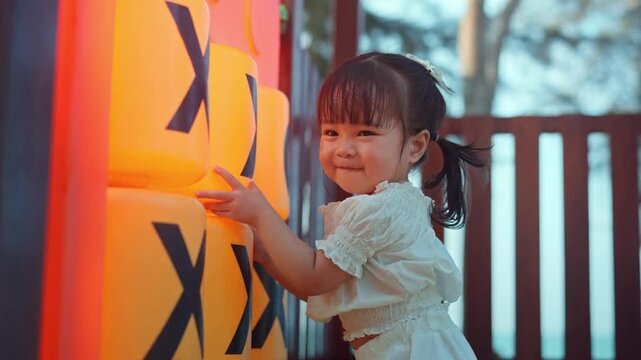 Happy Asian toddler girl laughing while playing with colorful outdoor playground equipment, cheerful little child enjoying active play, childhood fun, recreation, learning and healthy development
