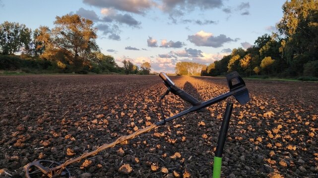 Metal detector resting on a plowed field during a golden hour sunset