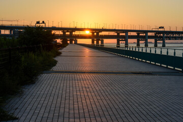 Obraz premium A serene urban promenade leading towards a massive sunset bridge over water.