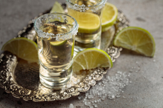 Tequila with salt and lime slices on a silver tray.