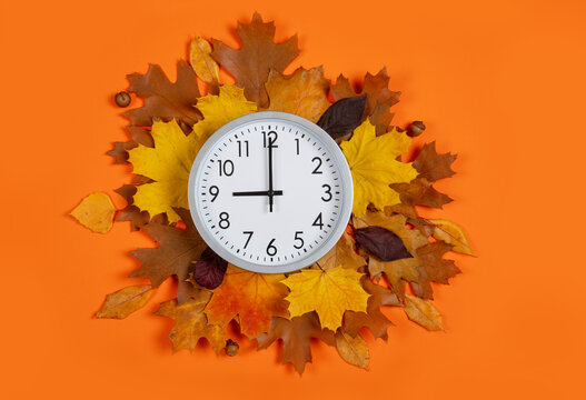 9 o'clock, round wall clock on autumn leaves wreath over orange background, daylight saving time concept. Conceptual flat lay composition for transition of the fall season, time management, fall sales