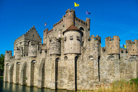 Medieval stone castle with moat and battlements stands against deep blue sky in Ghent