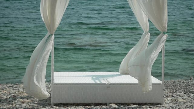Beach canopy bed, sea waves, white curtains blowing in wind on pebble shore