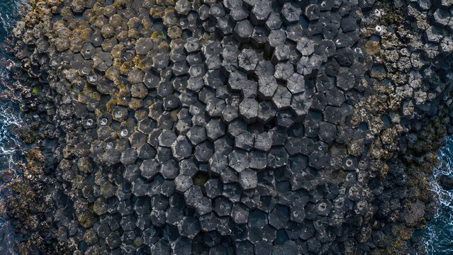 Aerial view of basalt columns forming natural hexagonal rock patterns on the coastline.