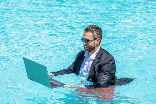 Fun business lifestyle. Businessman in suit with laptop in swimming pool. Crazy business man summer vacation. Remote working. Summer business vacation. Businessman rest in pool. Laptop on beach