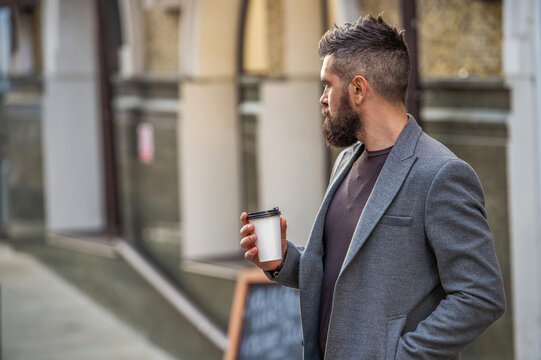 Bearded man having coffee in city street. Handsome man on street holding cup coffee. Business lifestyle, break. Man drinking morning coffee. Urban coffee lifestyle