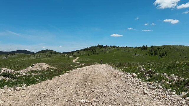 Female cyclist rides toward the camera on a gravel road across the Durmitor plateau in Montenegro. Great for travel, cycling and active tourism content