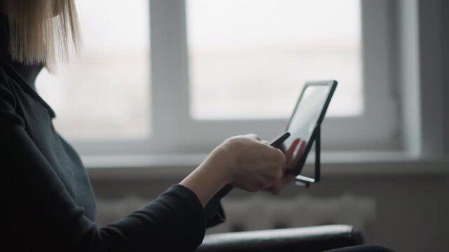 Close up of woman using digital drawing tools holding stylus and tablet in soft natural light. Digital art creation process visible with focused hand movements on device. Indoor workspace