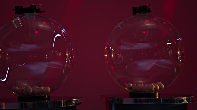 Lottery drawing transparent glass spheres with numbered white balls inside under dramatic red studio lighting
