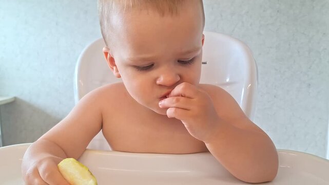 Toddler boy sitting in a high chair and eating a fresh apple slice