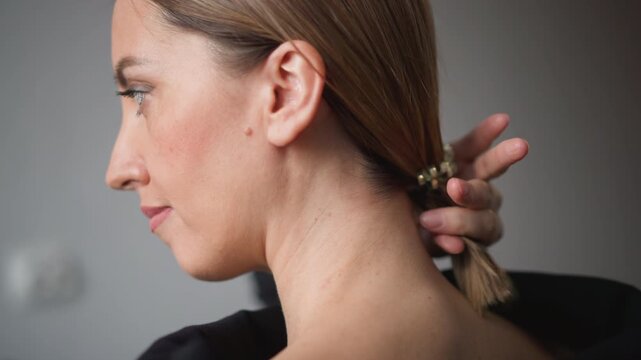 Close up of woman with light brown hair styled in low ponytail secured by beaded accessory. hand gently adjusts hairstyle revealing soft skin texture and natural facial features