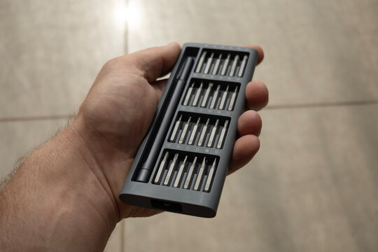 Hand holding a precision screwdriver set with bits in a gray case