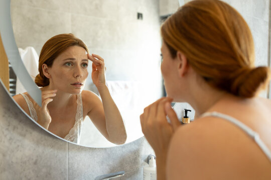 Woman noticing forehead wrinkles in bathroom mirror