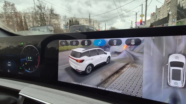Car parking system, 3d camera view displays vehicle position on digital display, aiding driver during city street maneuver. Static interior shot.