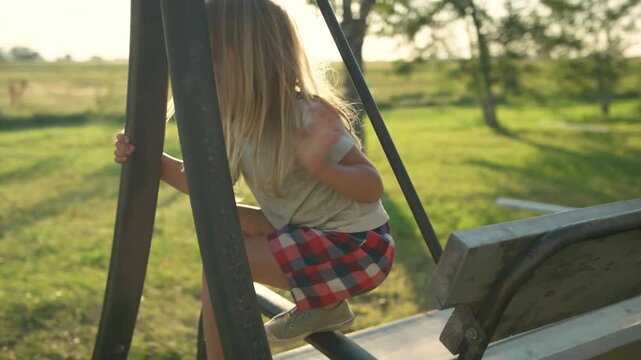 Boy playing on swing structure then gazing out across green field at sunset