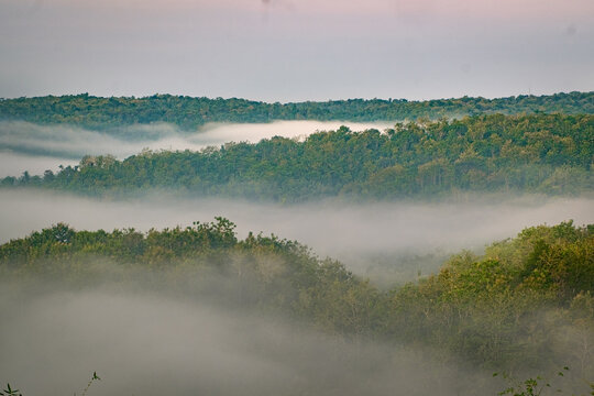 A beautiful view of green hills shrouded in thick morning mist, offering a lush and peaceful natural atmosphere&mdash;located at Gunung Ireng, Jogja, Indonesia