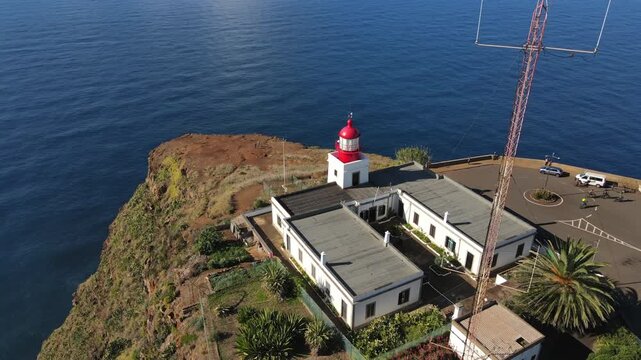 Stunning aerial footage showing the iconic Ponta do Pargo Lighthouse standing on the edge of a rugged cliff above the vast blue ocean