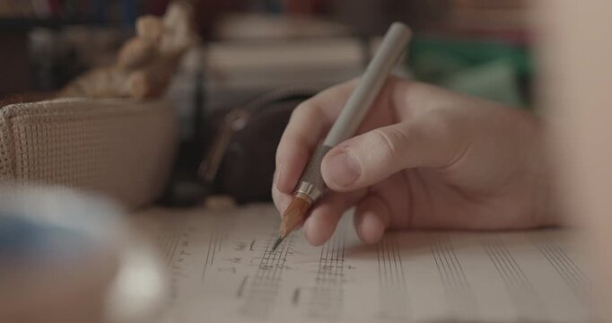 Cinematic close-up hand writing classical guitar music notation on sheet music with a pencil. Warm educational and creative atmosphere.