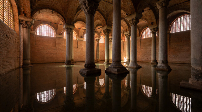 Illuminated capitals and columns inside ancient Byzantine cistern with calm water reflecting brick vaults