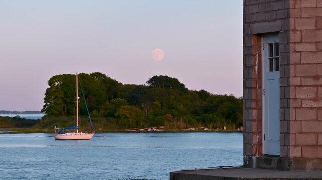 Groton, Connecticut, USA &ndash; Sturgeon Moon and Sailboat Framed by Avery Point Lighthouse