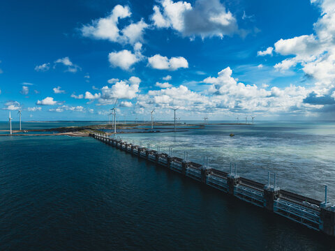 High angle wide horizontal aerial drone photograph of Oosterscheldekering storm surge barrier, offshore wind turbines, and North Sea horizon in Zeeland, Netherlands on sunny summer day