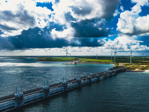 High angle wide horizontal aerial drone photograph of Oosterscheldekering storm surge barrier, wind turbines, Neeltje Jans island, and North Sea in Zeeland, Netherlands on sunny summer day