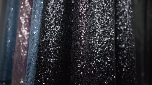 Close up of black sequin dress fabric with shimmering texture and soft lighting. Dress material displays sparkling details hanging vertically in fashion retail setting. Background includes