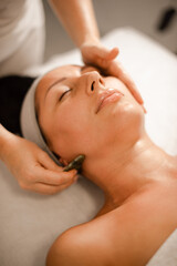 Professional masseuse performing gua sha facial massage with jade stone tool in spa salon © cenchild