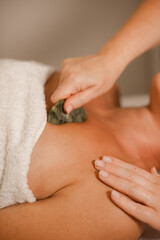 Beautician using gua sha jade stone scraper on woman chest and decollete in spa salon © cenchild