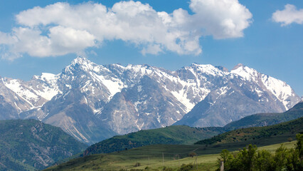 Naklejka premium Snow-capped mountains rise above green valleys