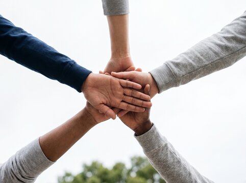 Diverse group of people stacking hands together to show unity and collaboration in bright daylight