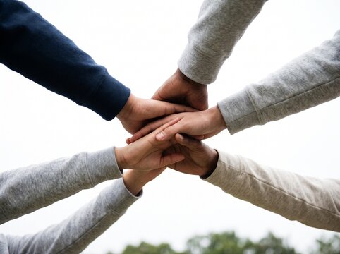 Diverse group of people stacking hands together to show unity and collaboration in bright daylight