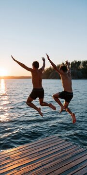 Two friends jumping off a wooden dock into a lake at sunset for summer adventure background and outdoor lifestyle banner